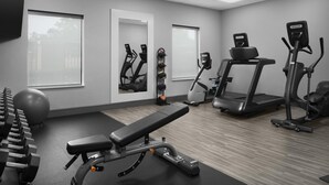 Un gimnasio con equipo de ejercicio, una banca y ventanas amplias.