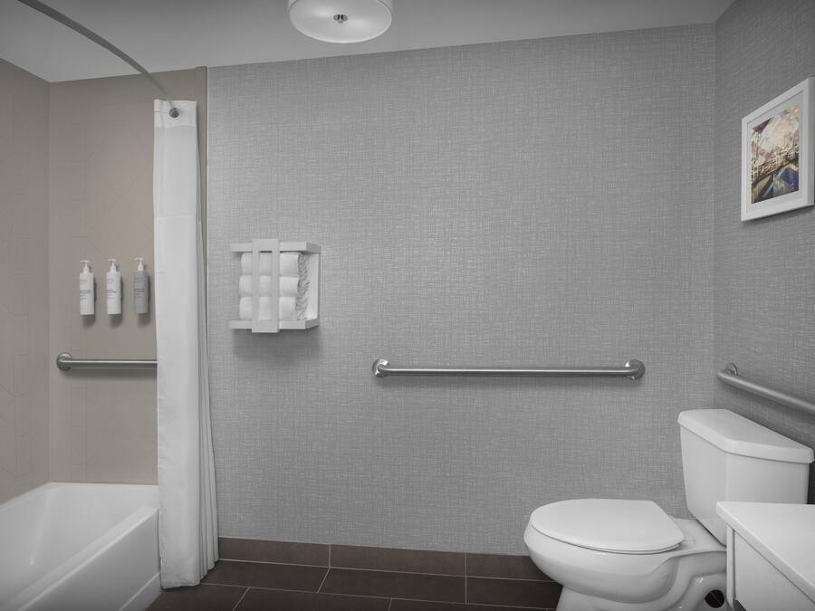 A modern bathroom with a bathtub, toilet, and shower. There are handrails and a towel rack on the wall.
