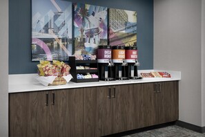 A counter with coffee dispensers, snacks, and a decorative wall with cityscape artwork. - Hampton Inn & Suites Jacksonville South - Bartram Park (Jacksonville)