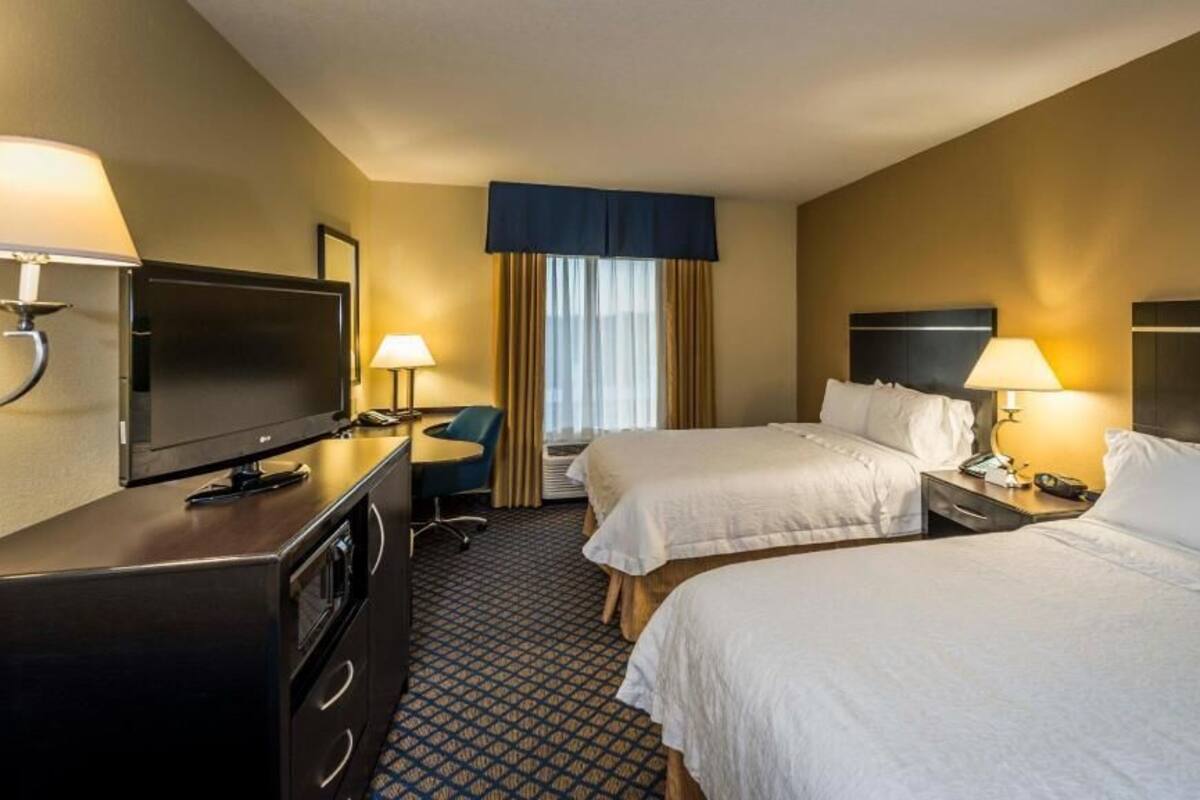A hotel room with two beds, a desk with a television, and a chair.