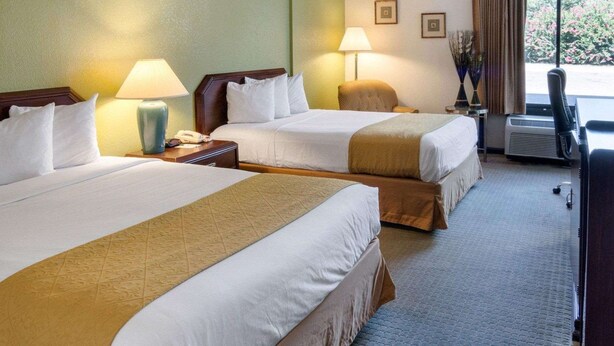 A hotel room with two beds, a desk, a chair, a lamp, and a view of the outdoors. - Quality Inn Shreveport Airport (Shreveport)