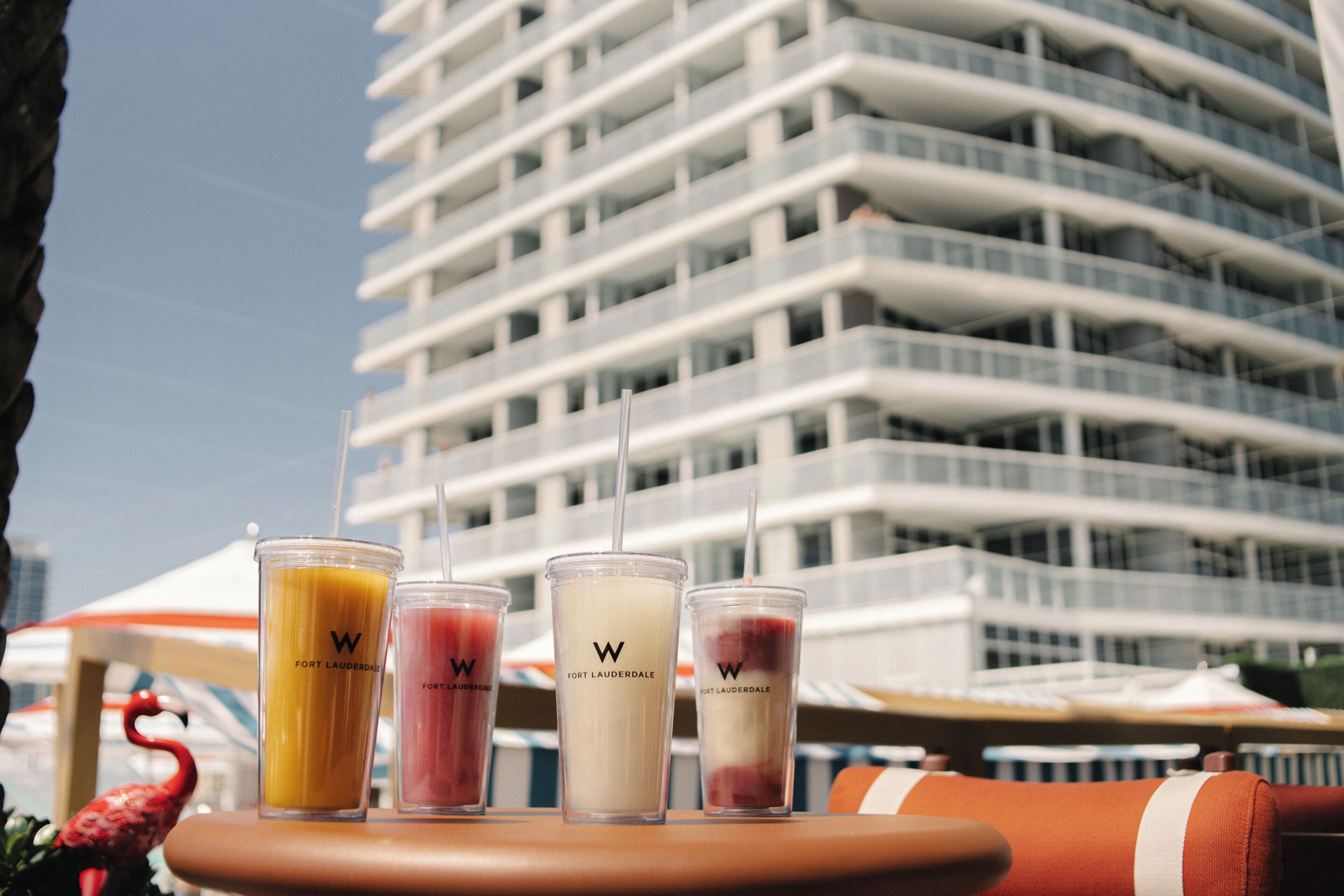 A table with four beverage containers, a red flamingo decoration, and a modern building in the background.