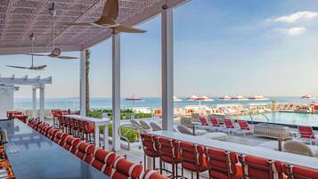 Un espace aménagé au bord de la piscine, avec un long bar, des sièges rouges et blancs et des parasols.