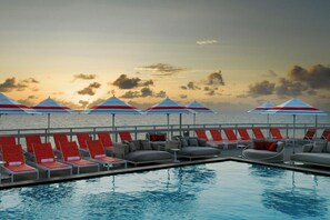 A poolside area with lounge chairs and umbrellas, overlooking a body of water at sunset. - W Fort Lauderdale (Fort Lauderdale)