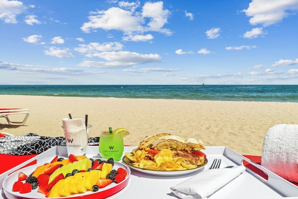 Una mesa en la playa con comida, bebida y una toalla.