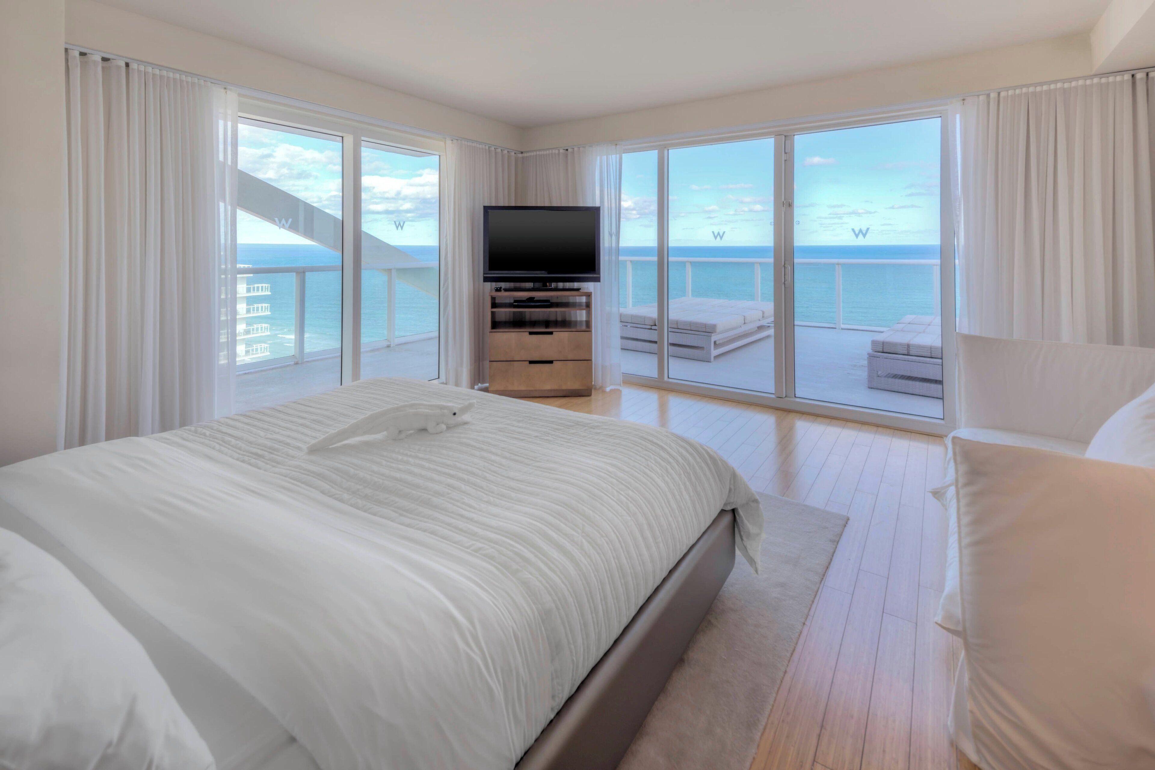 A spacious bedroom with a large bed, a television, and a balcony with a view of the sea.