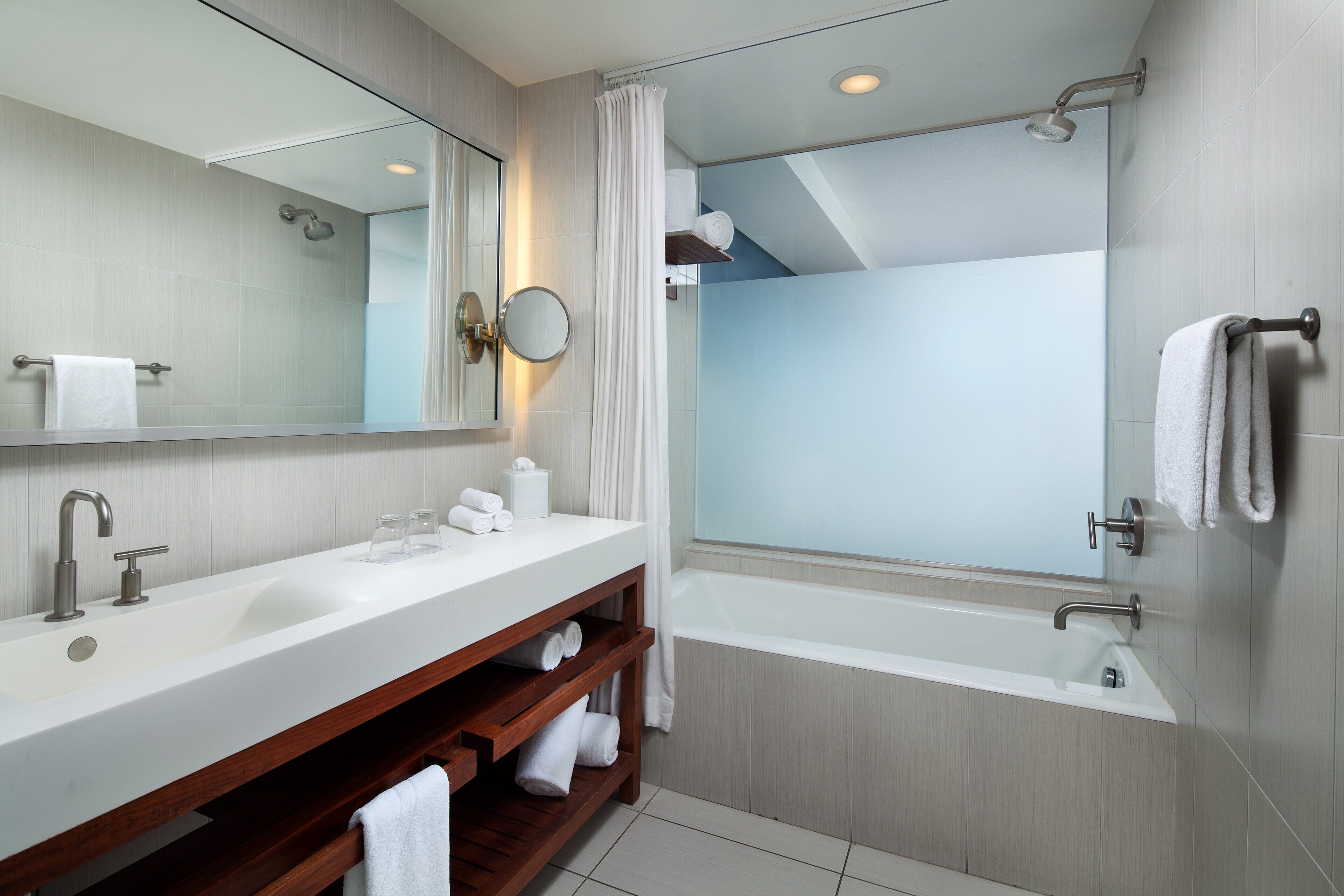Un baño moderno con un espejo grande, un lavamanos, una ducha y una bañera.