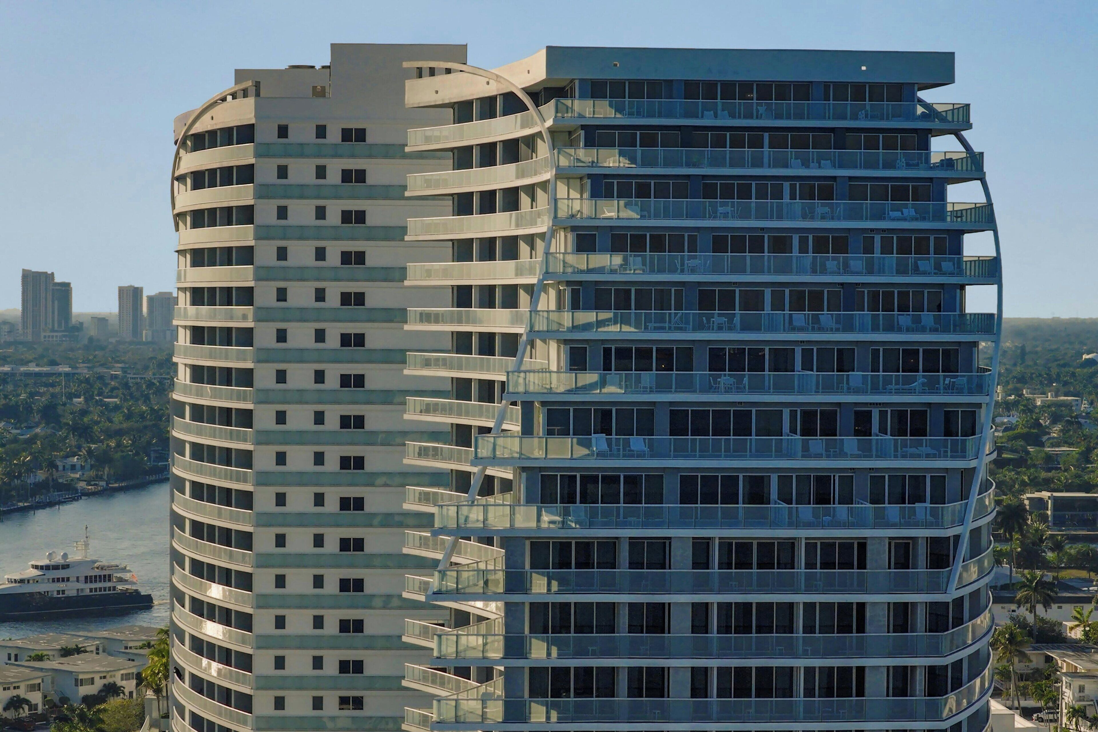 A modern high-rise building with multiple balconies and large windows, overlooking a river and cityscape.