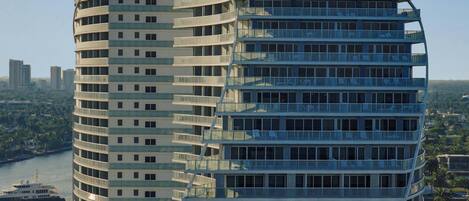A modern high-rise building with multiple balconies and large windows, overlooking a river and cityscape.