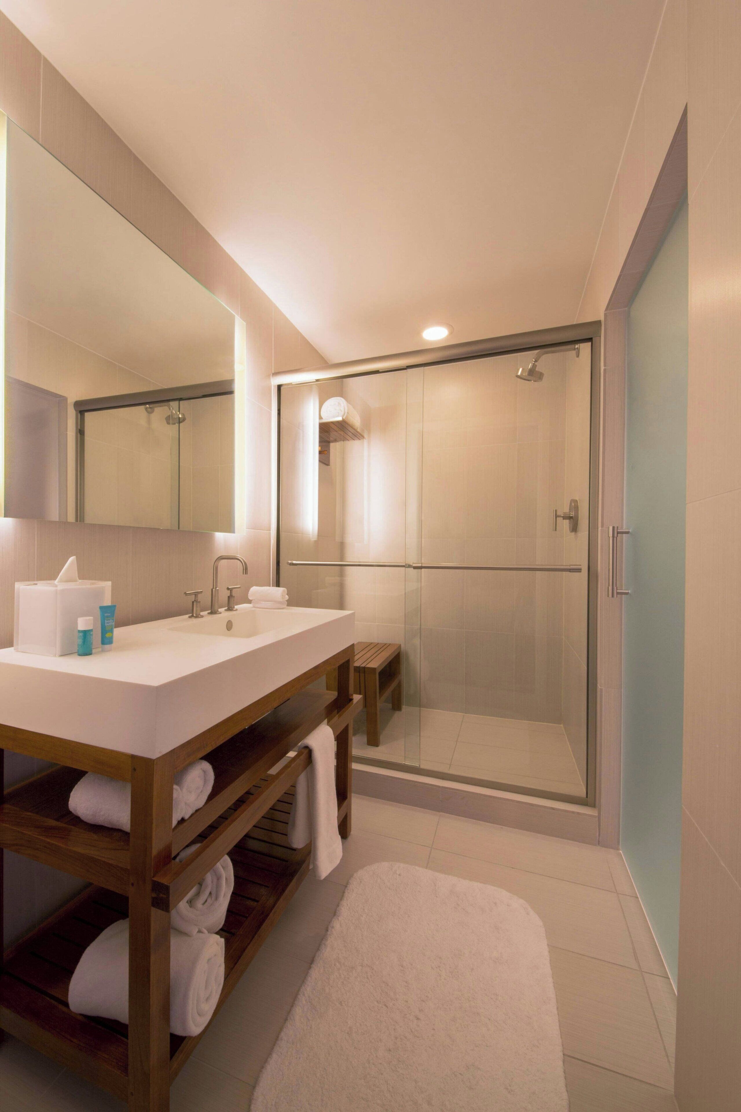 A modern bathroom with a large mirror, two sinks, a shower enclosure, and a wooden vanity with towels.