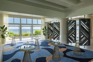 A spacious lobby with large windows offering a view of the sea, a blue patterned carpet, and modern glass tables.