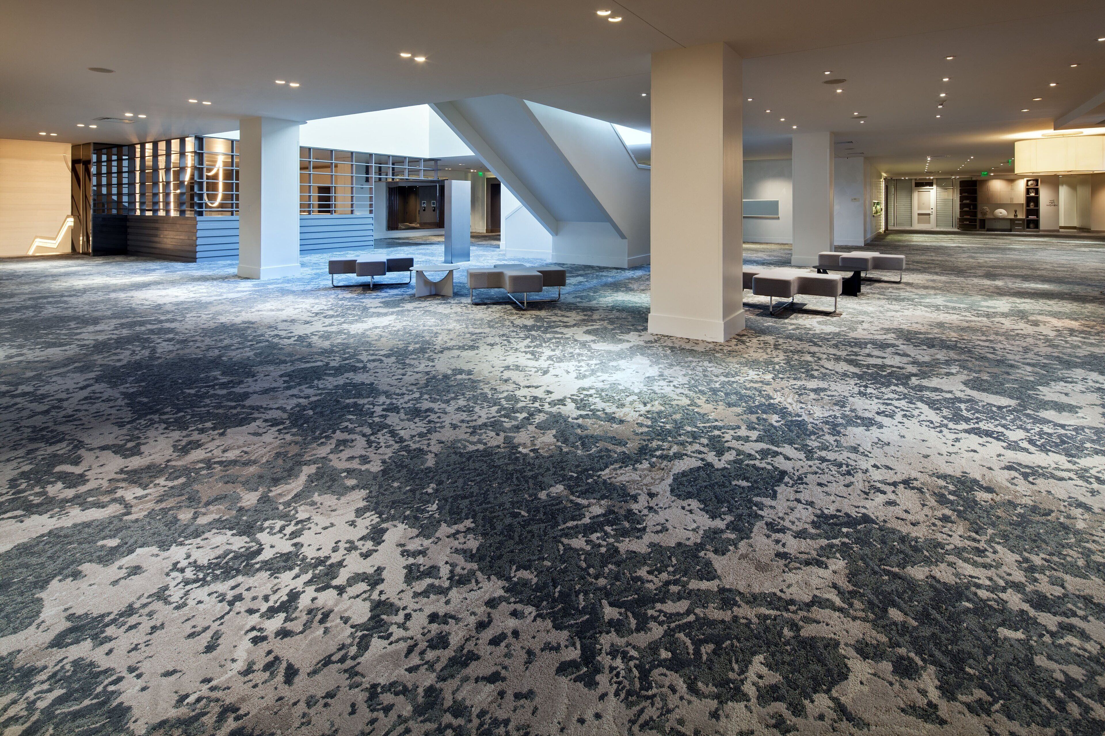 Un vaste espace intérieur doté d’un tapis à motifs, de différents coins salon et d’un escalier.
