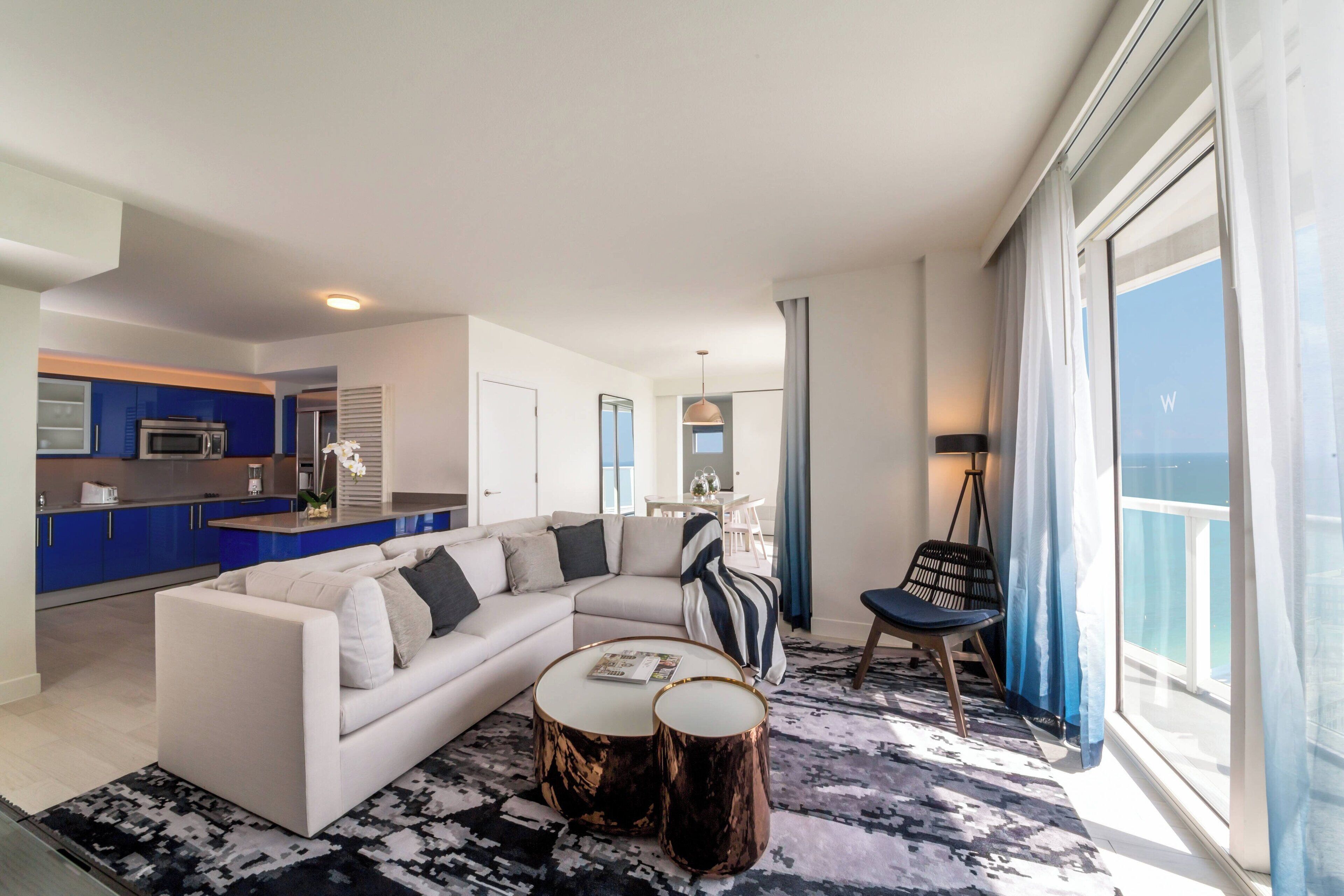 Ein modernes Wohnzimmer mit einem weißen Sofa, einem Couchtisch und einem Essbereich mit blauer Küche.