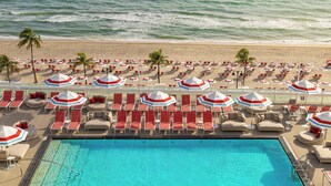 A poolside area with lounge chairs and umbrellas, a pool, and a beach in the background. - W Fort Lauderdale (Fort Lauderdale)