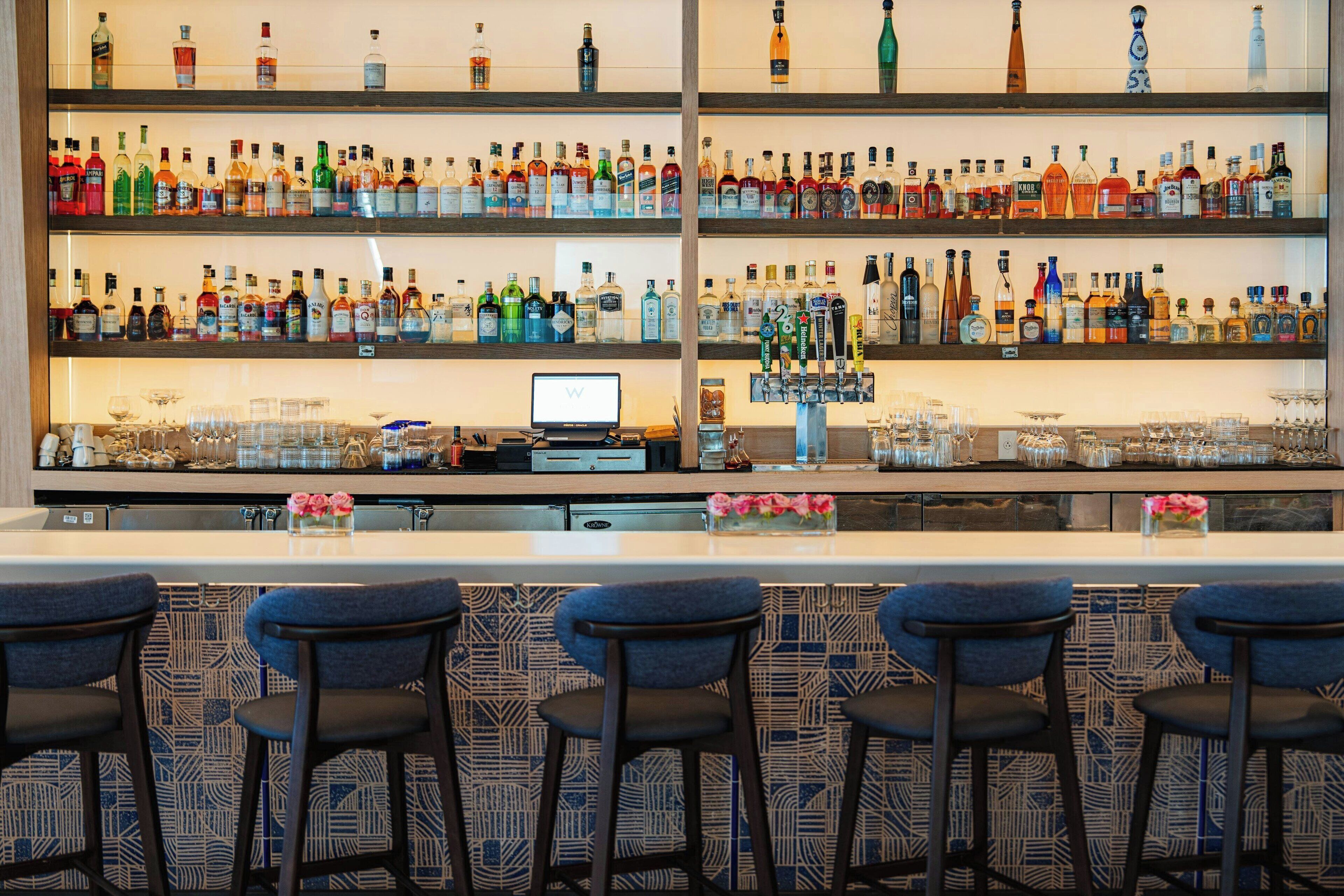 Un'area bar con numerose bottiglie di liquori sugli scaffali, un bancone e quattro sgabelli da bar.