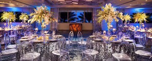 A banquet hall with round tables, clear chairs, and floral centerpieces.