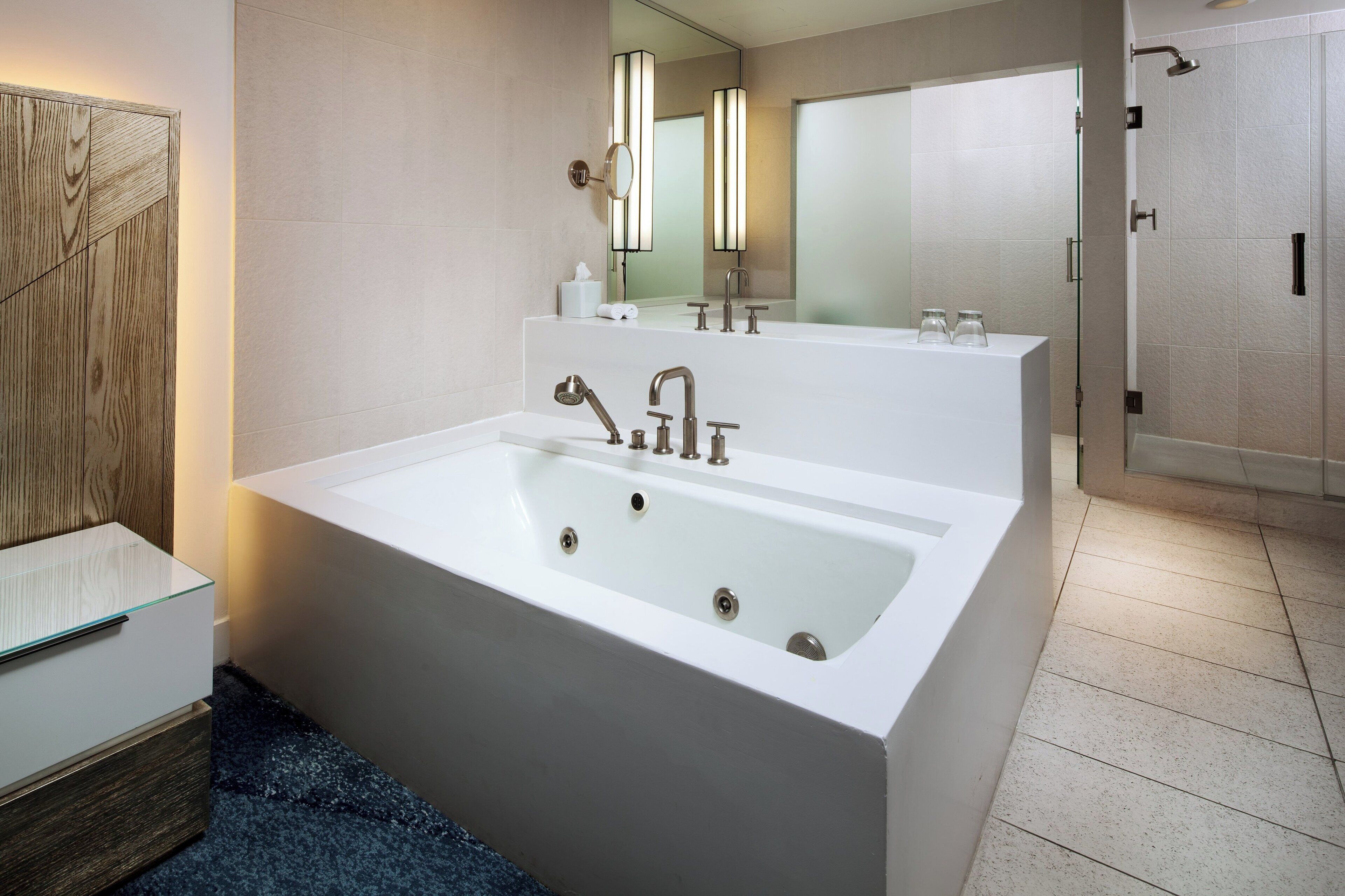 A modern bathroom with a large white bathtub, a glass-enclosed shower, and a wooden vanity with a mirror.