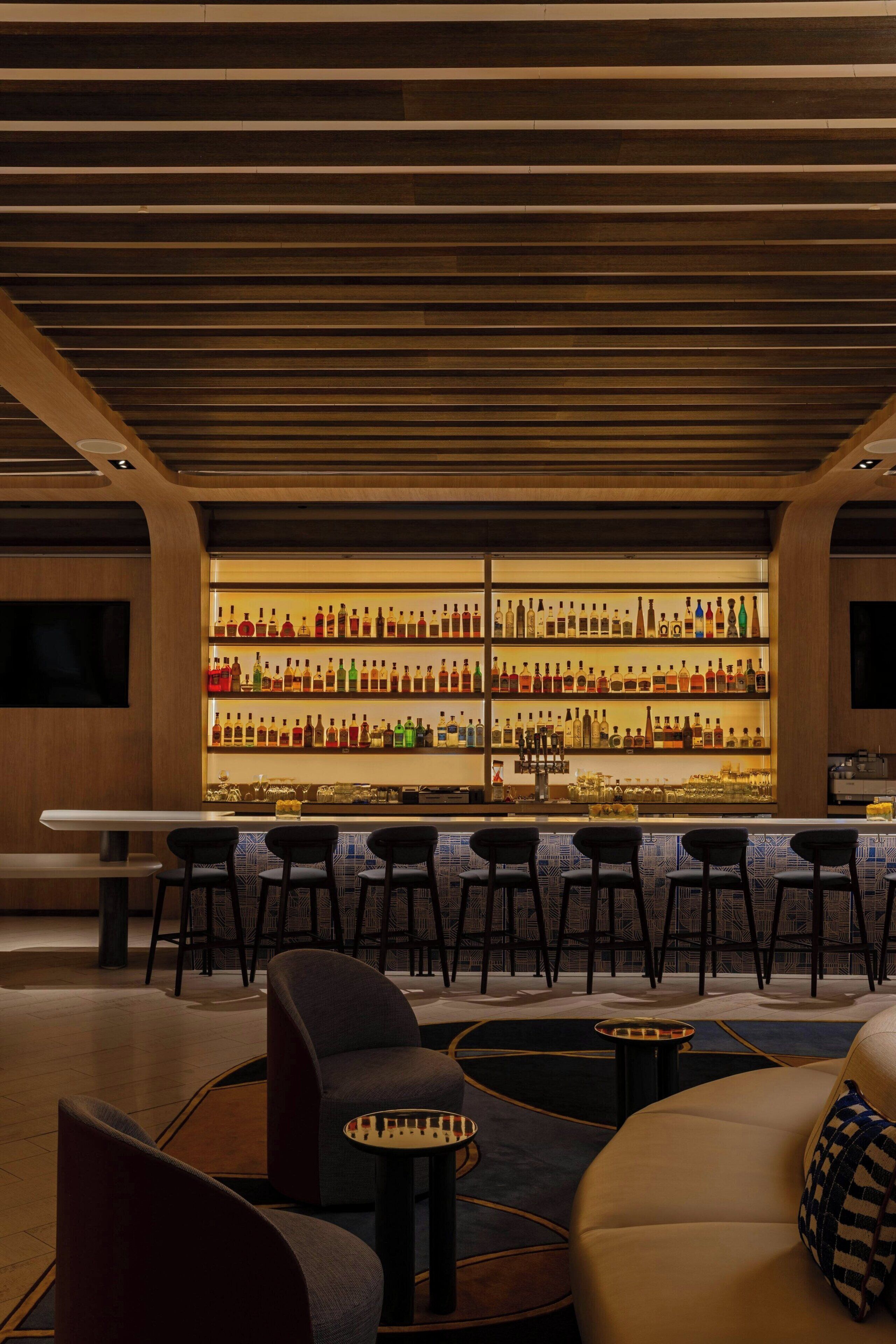 A bar area with a long counter, multiple chairs, and a sofa.