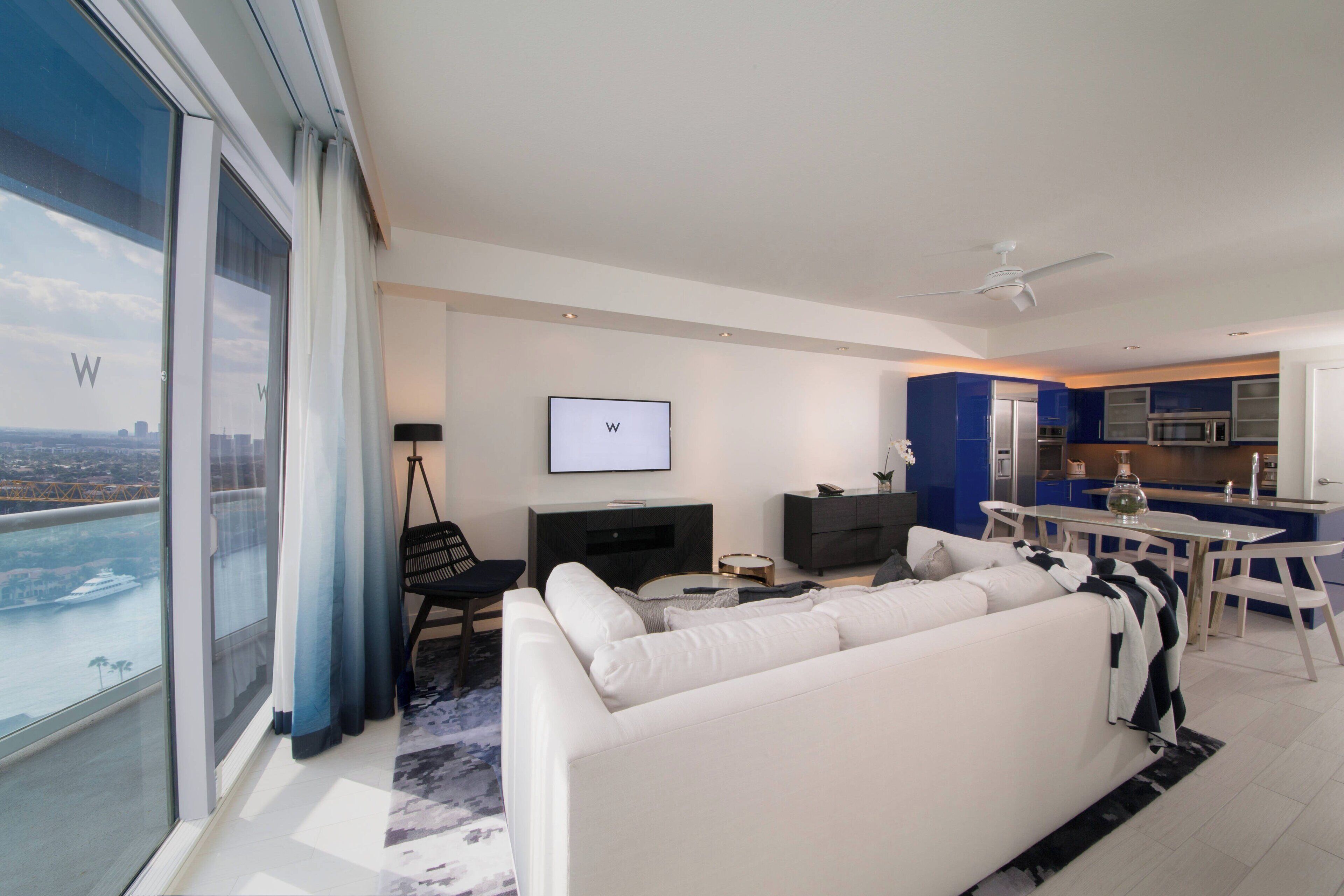 A modern living room with a white sofa, a flat-screen TV, and a dining area with a table and chairs.