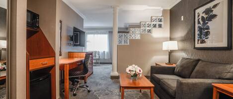 Una habitación de hotel con kitchenette, sofá, escritorio y mesa de centro.