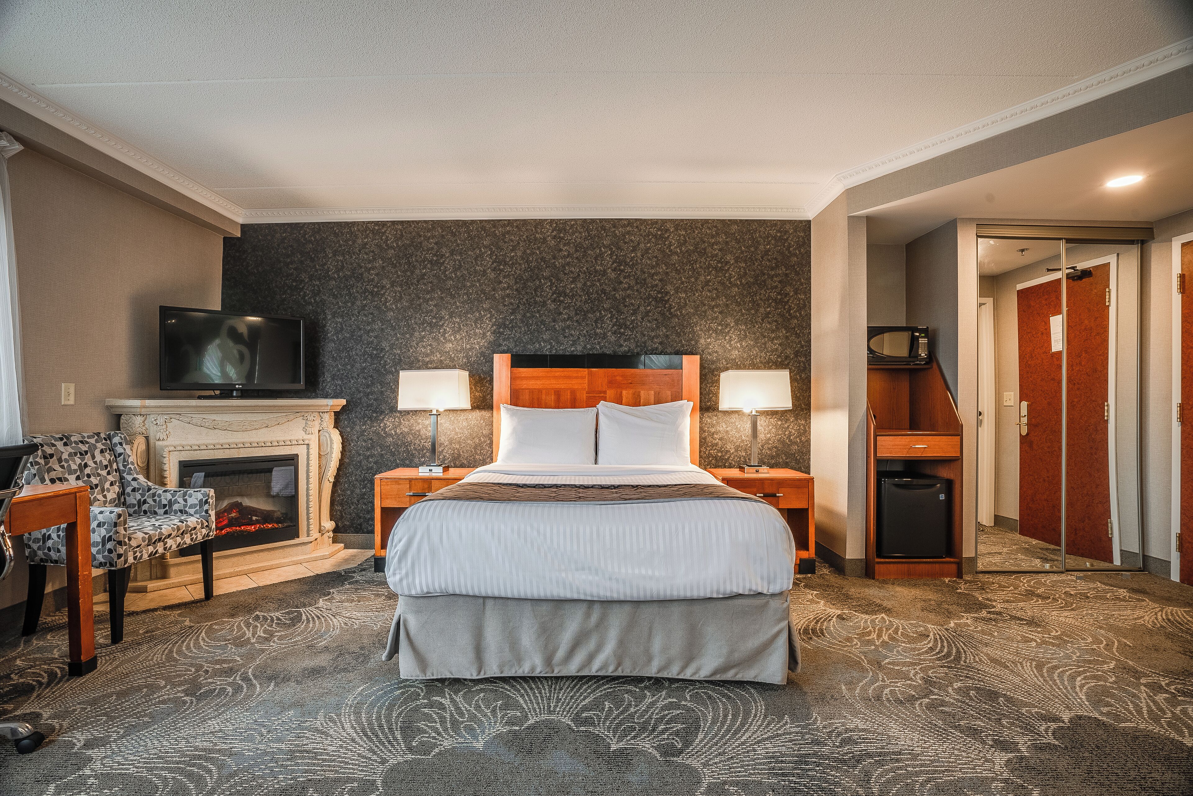 Una habitación de hotel con una cama grande, televisión, chimenea y escritorio con lámpara.