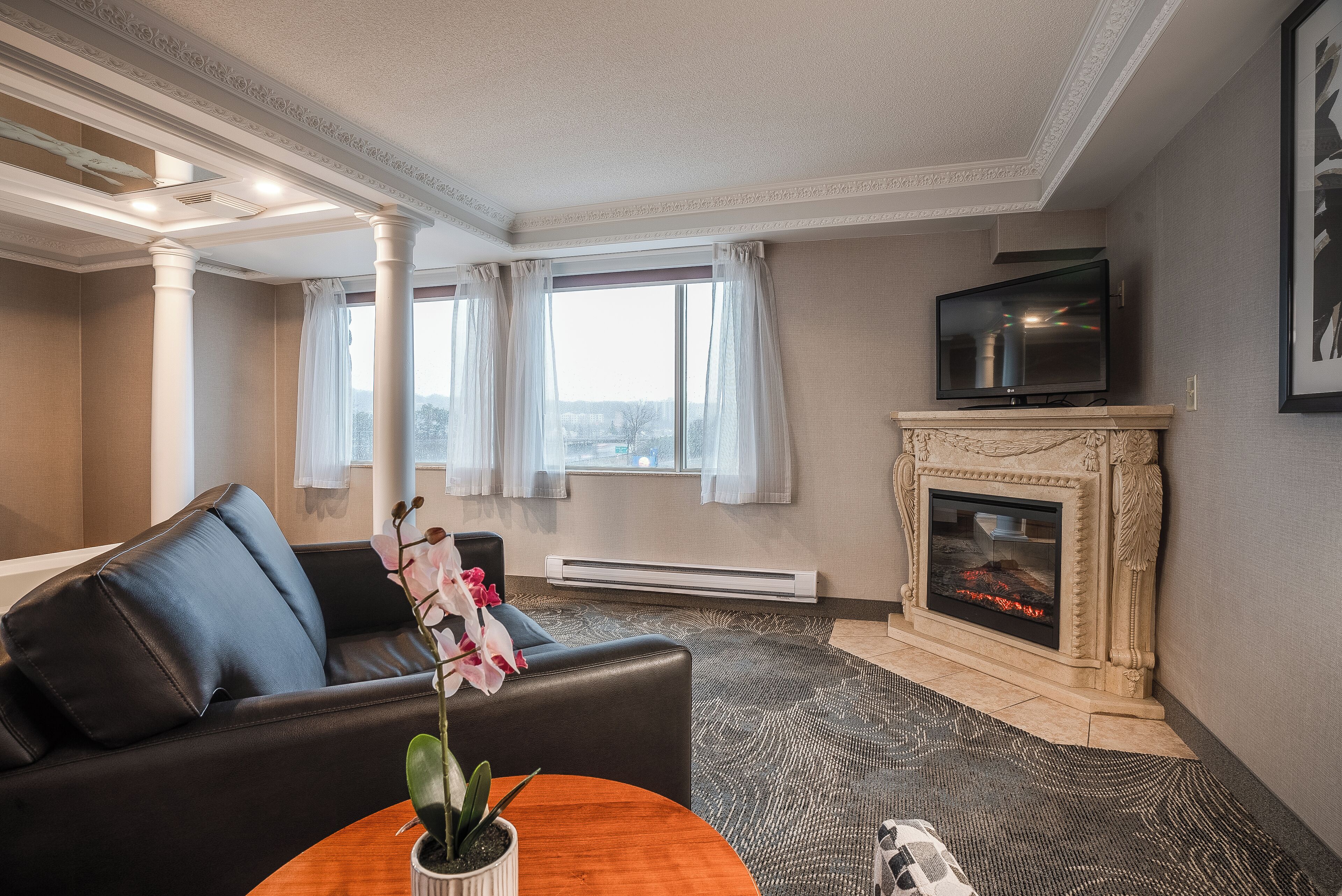 A living room with a fireplace, a television, and a sofa with a potted orchid.