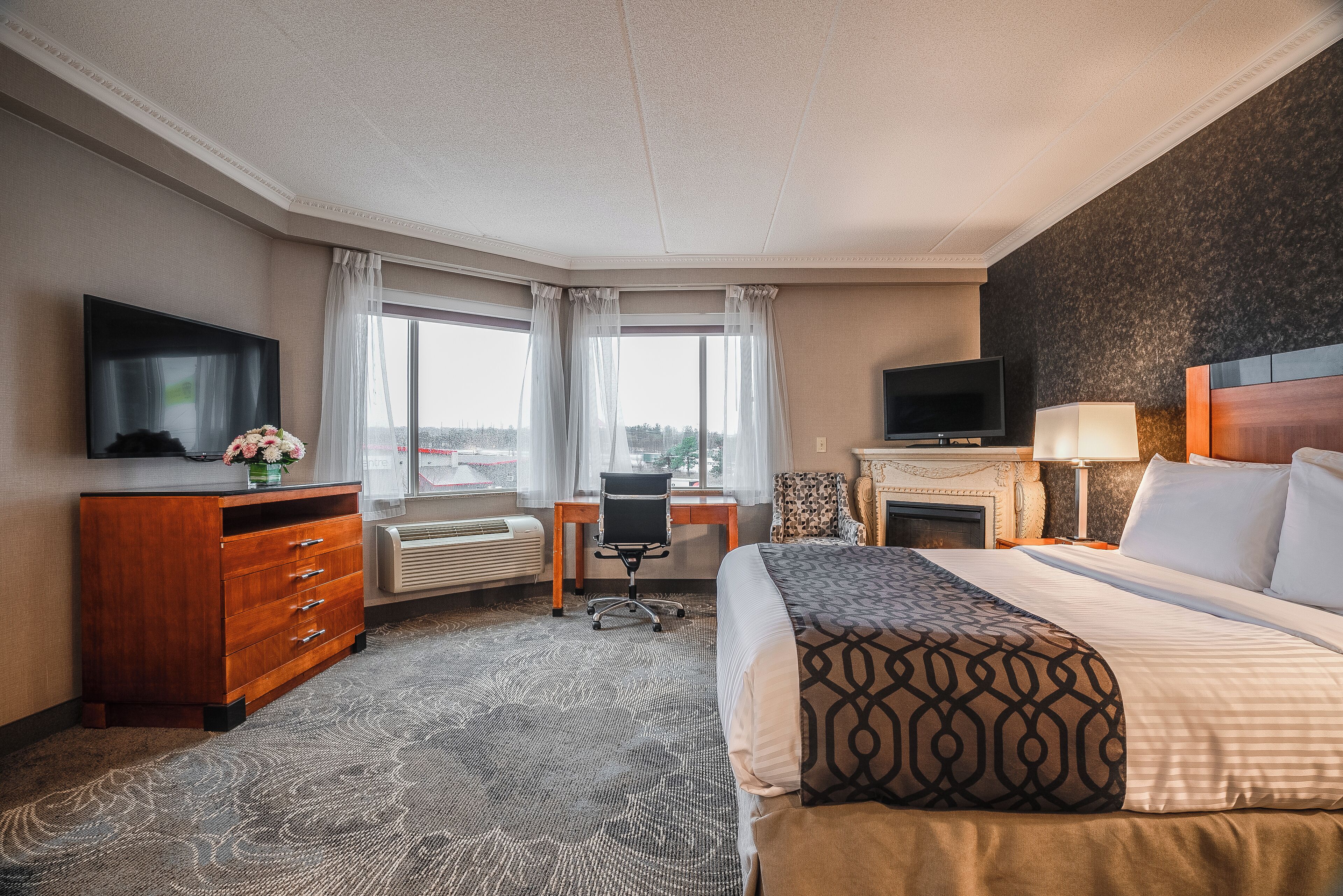 A hotel room with a bed, a desk, a TV, a dresser, and a fireplace.