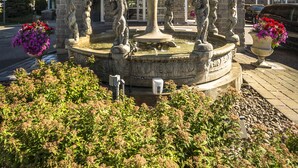 Una fuente con estatuas, rodeada de vegetación y un edificio con tejado de baldosas al fondo.