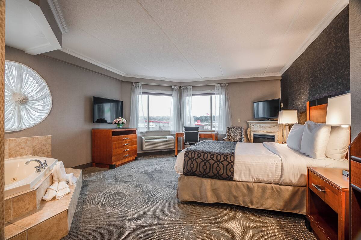 A hotel room with a large bed, a desk, a TV, a fireplace, and a view of the city.