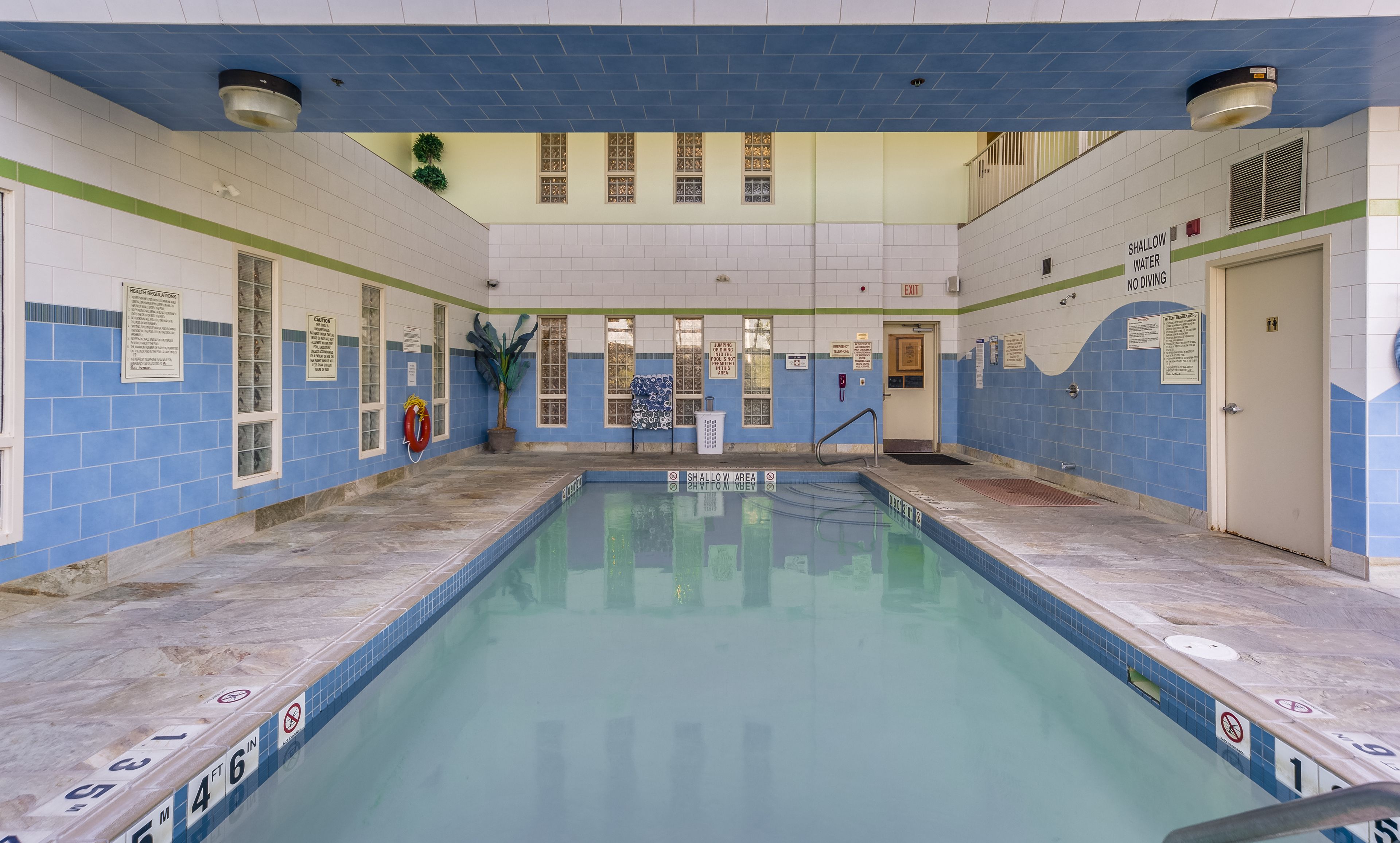 An indoor swimming pool with tiled walls, a shallow water sign, and a no diving sign.