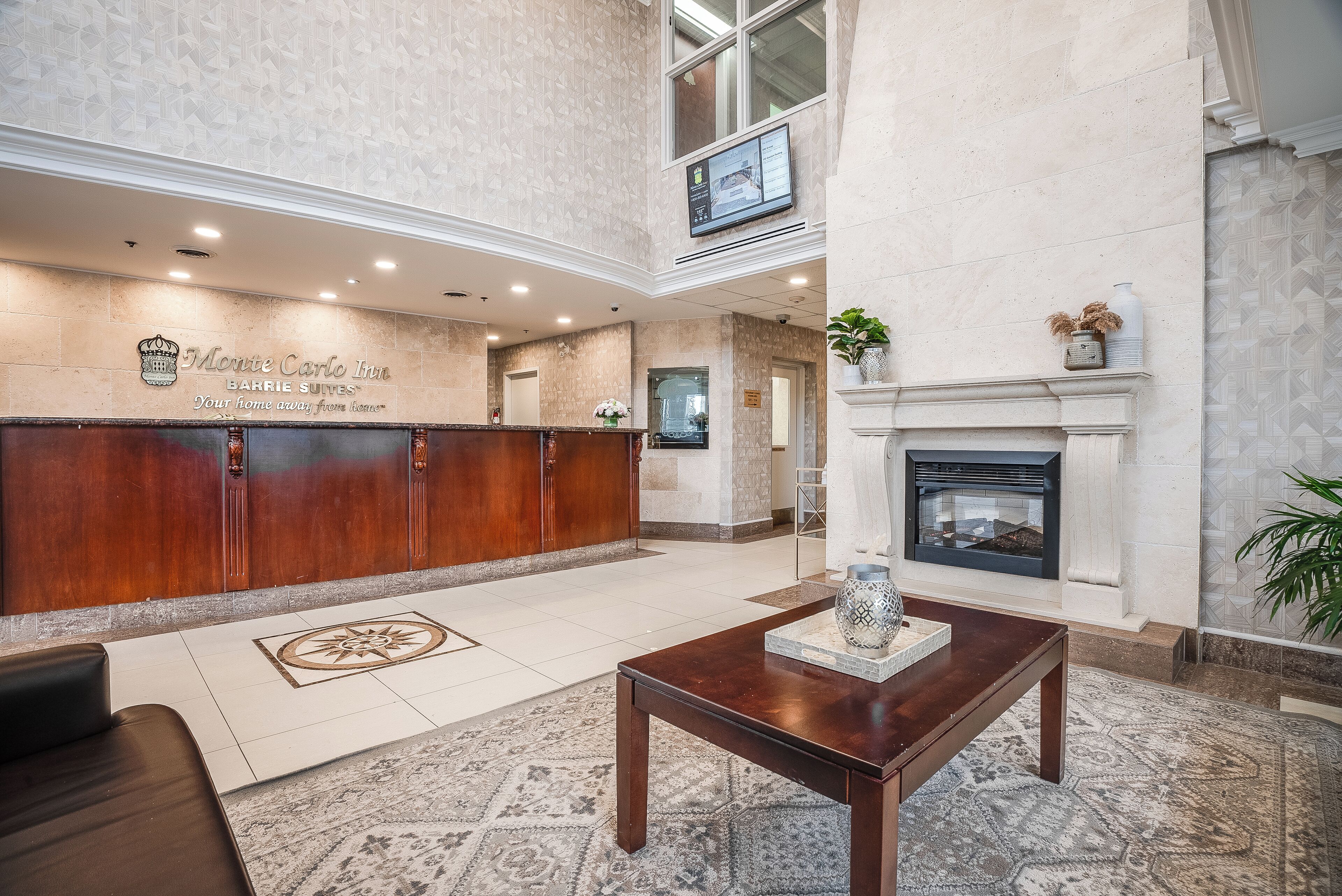 A hotel lobby with a reception desk, a fireplace, and a large rug.