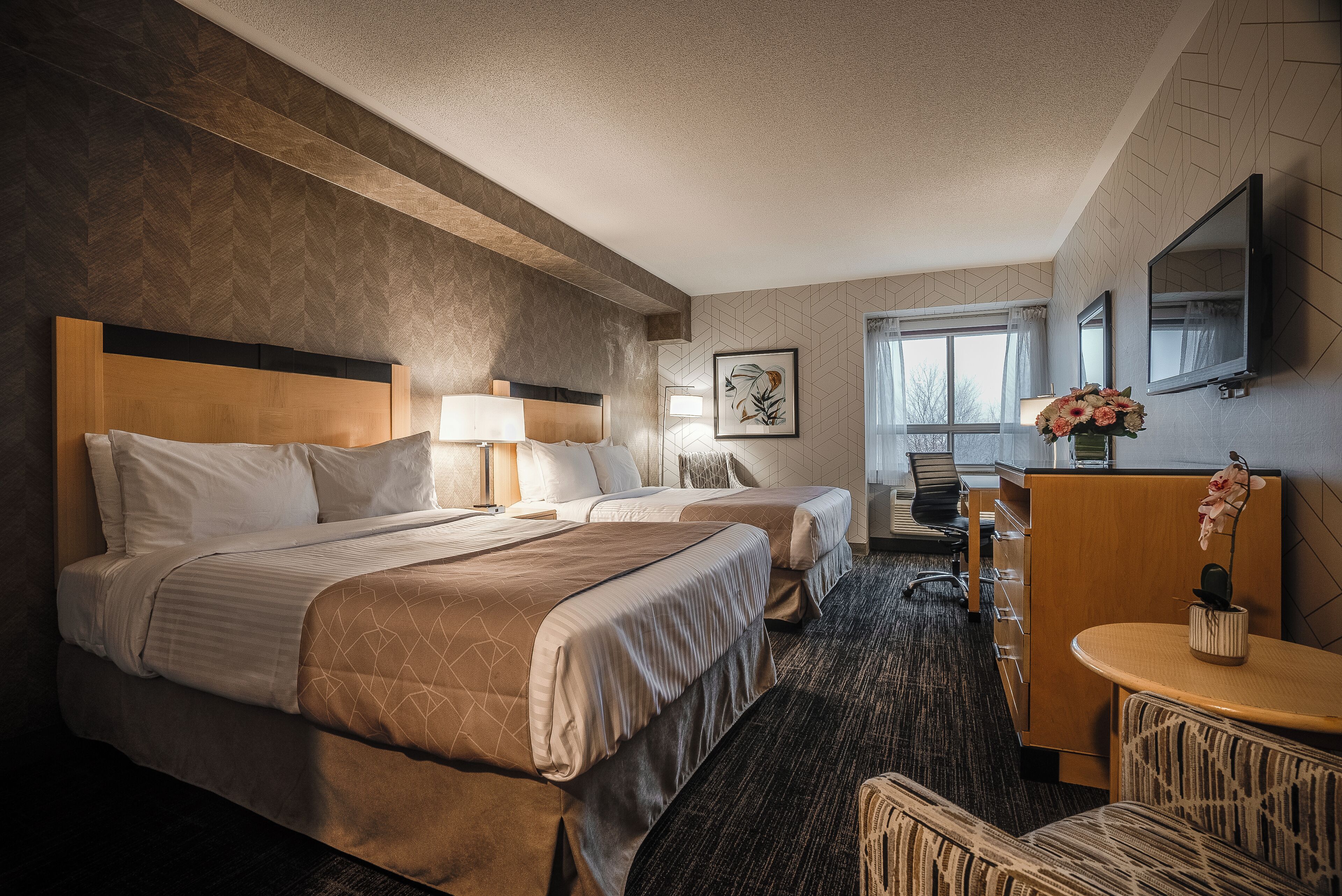 A hotel room with two beds, a desk, a chair, a TV, and a window with curtains.