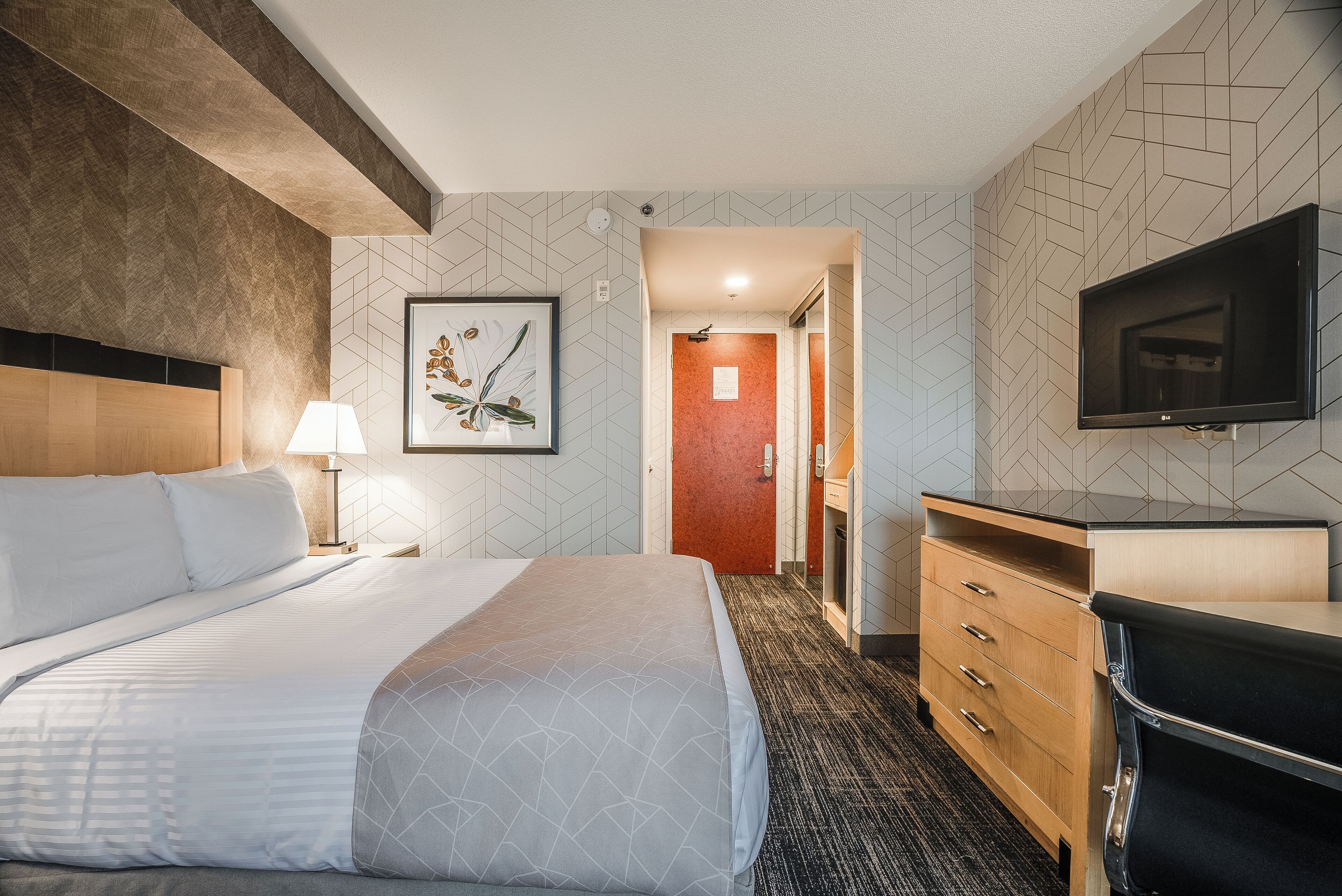Ein Hotelzimmer mit Bett, Schreibtisch, Fernseher und einem gerahmten Bild an der Wand.
