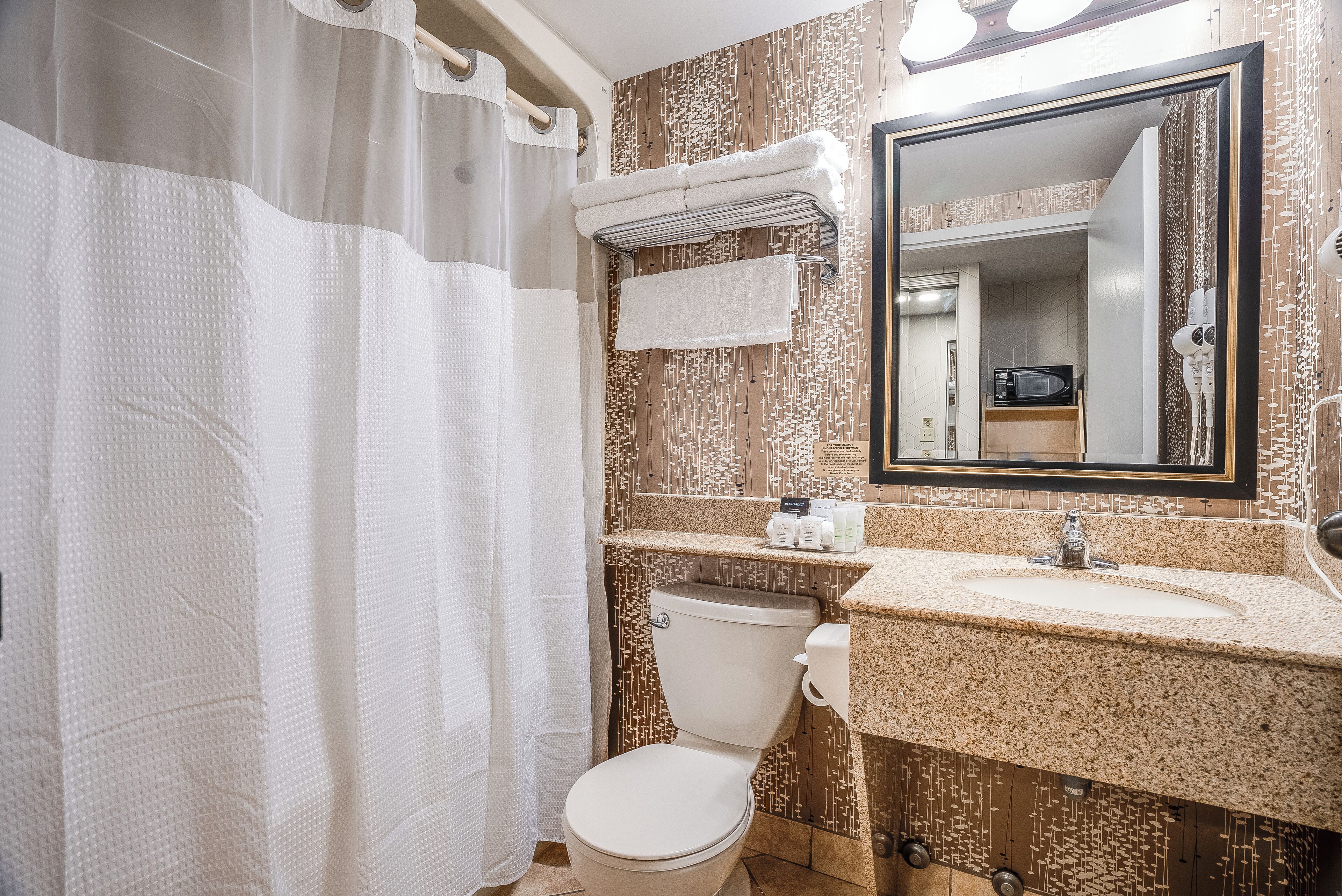 Une salle de bain avec un rideau de douche, des toilettes, un lavabo avec un miroir et un porte-serviettes.