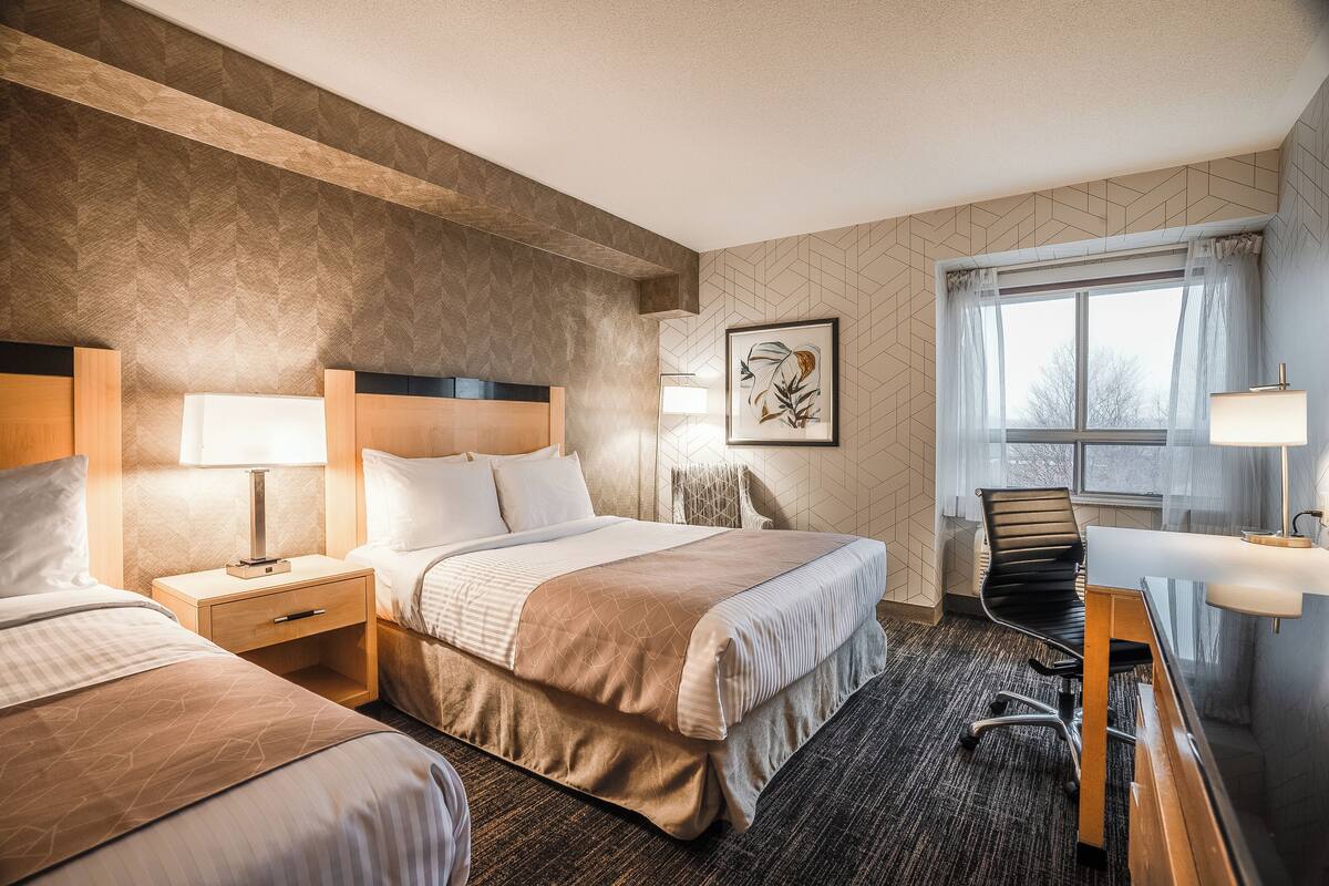 A hotel room with two beds, a desk, a chair, and a window with curtains.