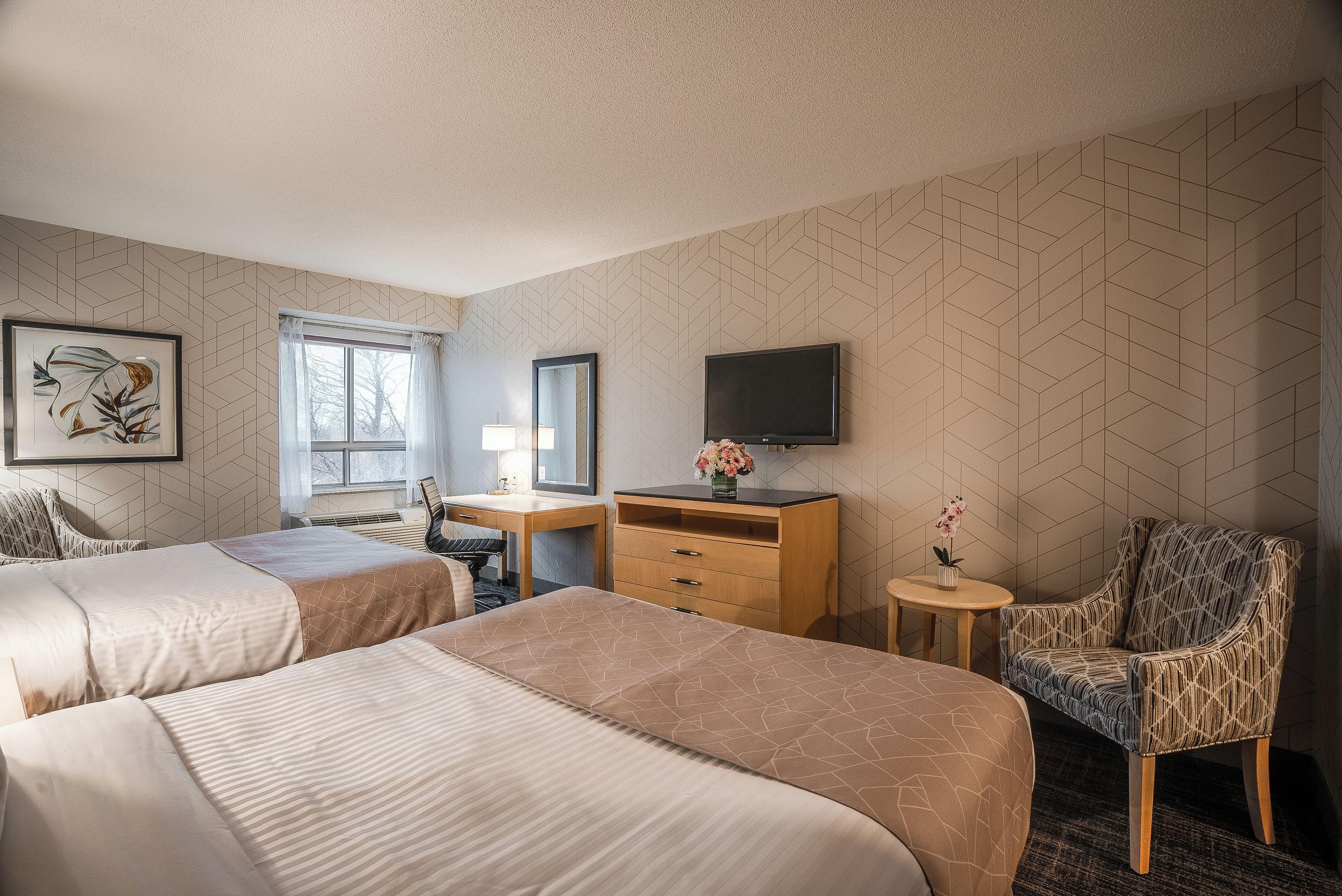 A hotel room with two beds, a desk, a chair, a TV, and a window.