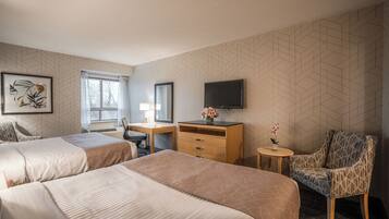 A hotel room with two beds, a desk, a chair, a TV, and a window.