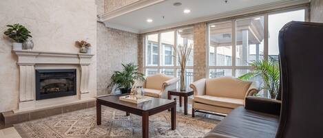 A spacious living room with a fireplace, beige sofas, a coffee table, and large windows offering a view of the city.