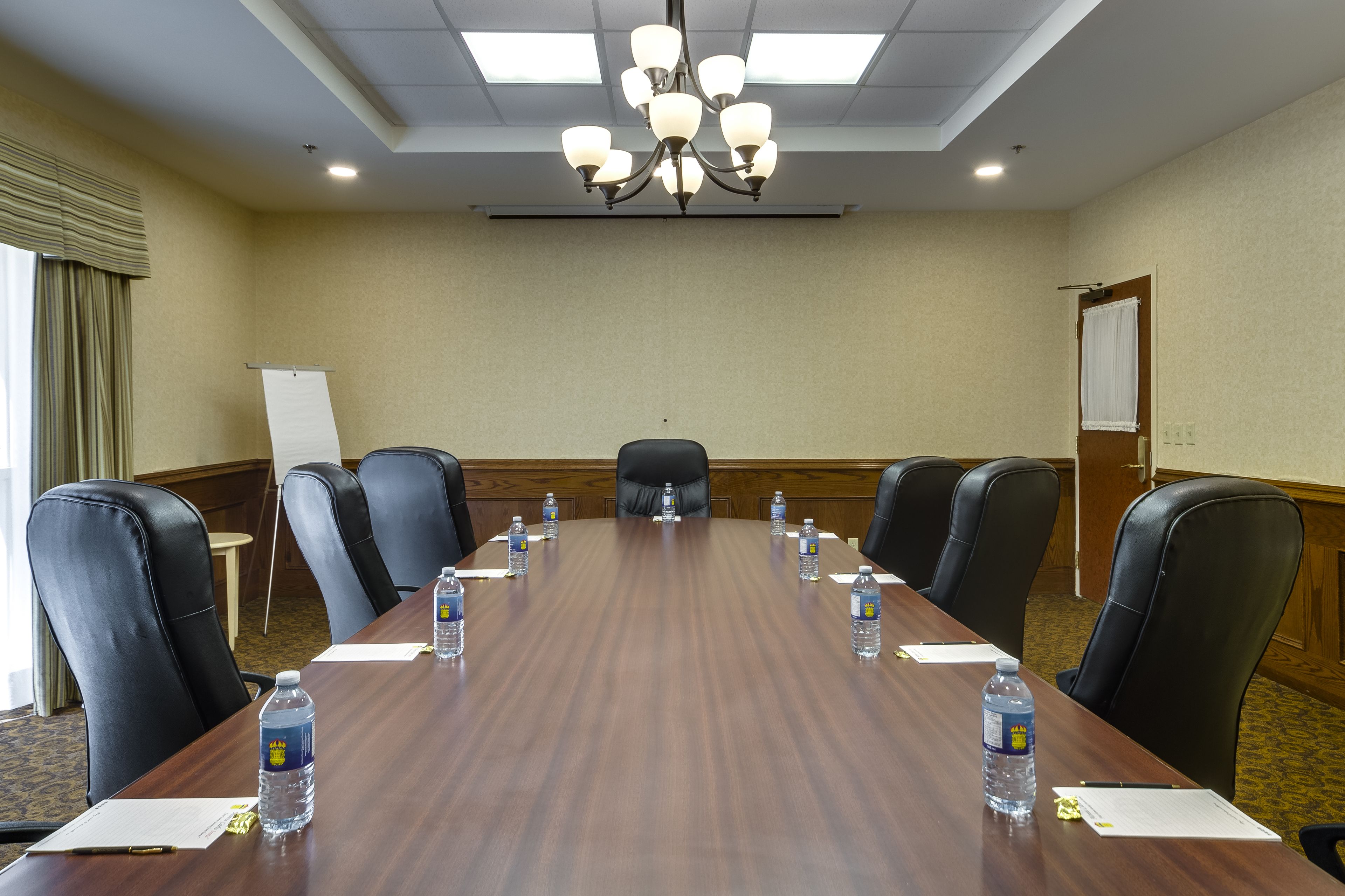 A conference room with a long wooden table, black leather chairs, water bottles, and a whiteboard.