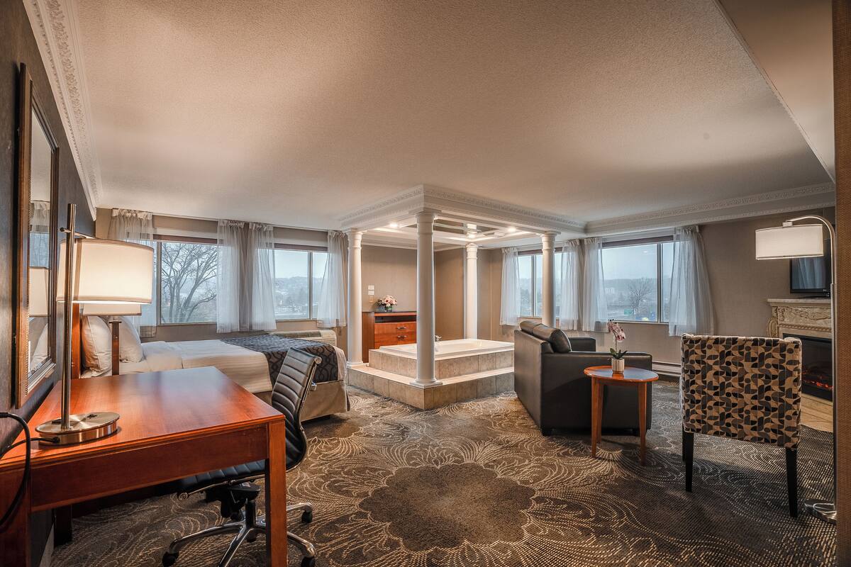 A hotel room with a bed, desk, chair, and a small seating area.