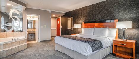 Een hotelkamer met een groot bed, een houten nachtkastje, een spiegel, een badkamer met een bad en een kamerbreed tapijt.