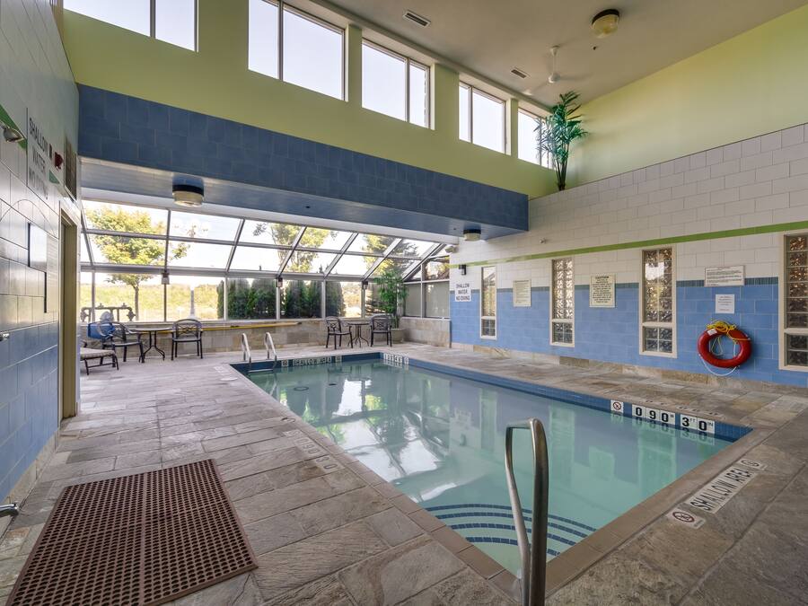 An indoor swimming pool with clear markings, a lifeguard chair, and a seating area with tables and chairs.