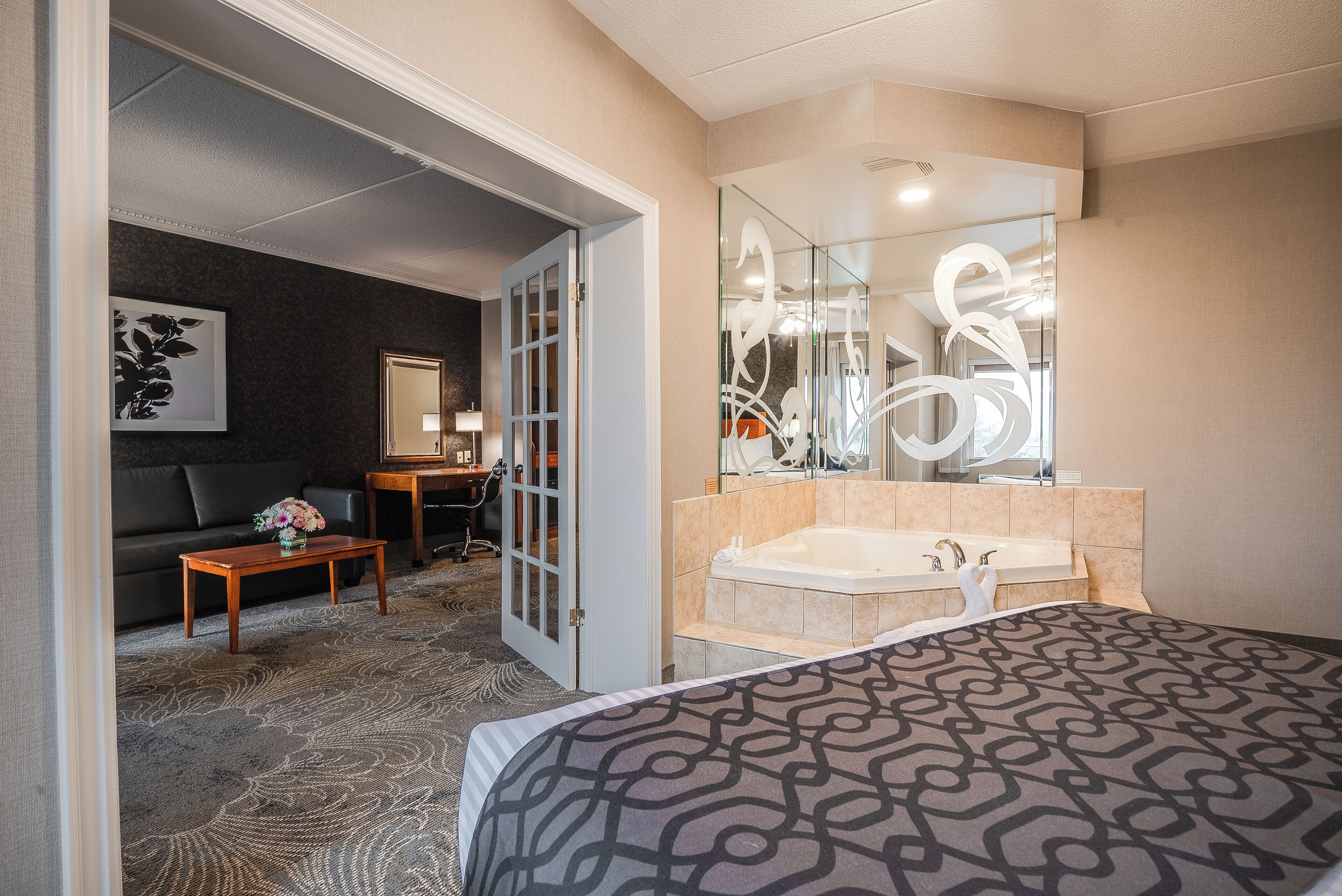 A hotel room with a large bed, a sitting area with a sofa and a small table, a bathroom with a bathtub and a large mirror.