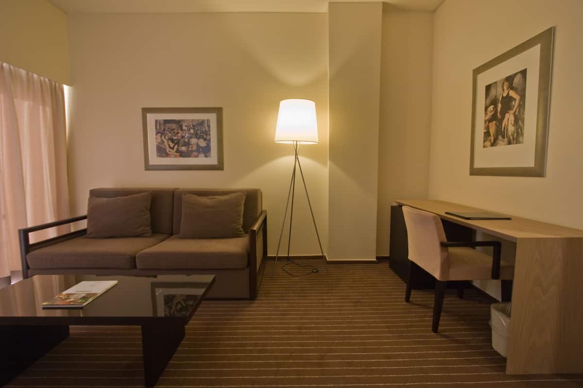 Et hotelværelse med sofa, skrivebord, lampe og billeder på væggene.