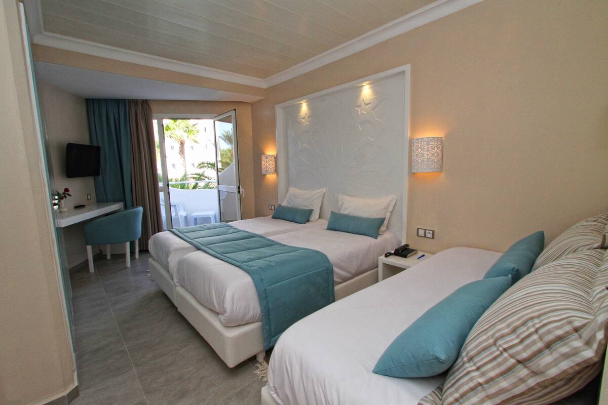 Quarto de hotel com duas camas, uma escrivaninha e uma cadeira.