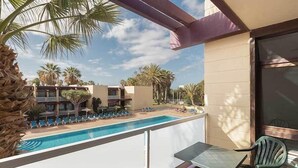 Un balcón con piscina, palmeras y vistas a edificios de hotel.