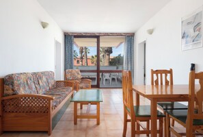 A room with a sofa, a dining table, and chairs, a balcony with a view of palm trees and buildings, and a painting on the wall. - Palia Don Pedro (Arona)