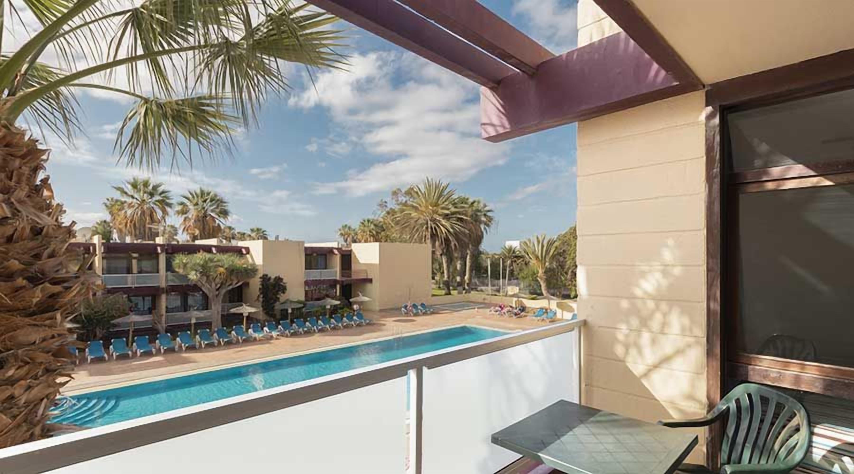 Un balcón con piscina, palmeras y vistas a edificios de hotel.