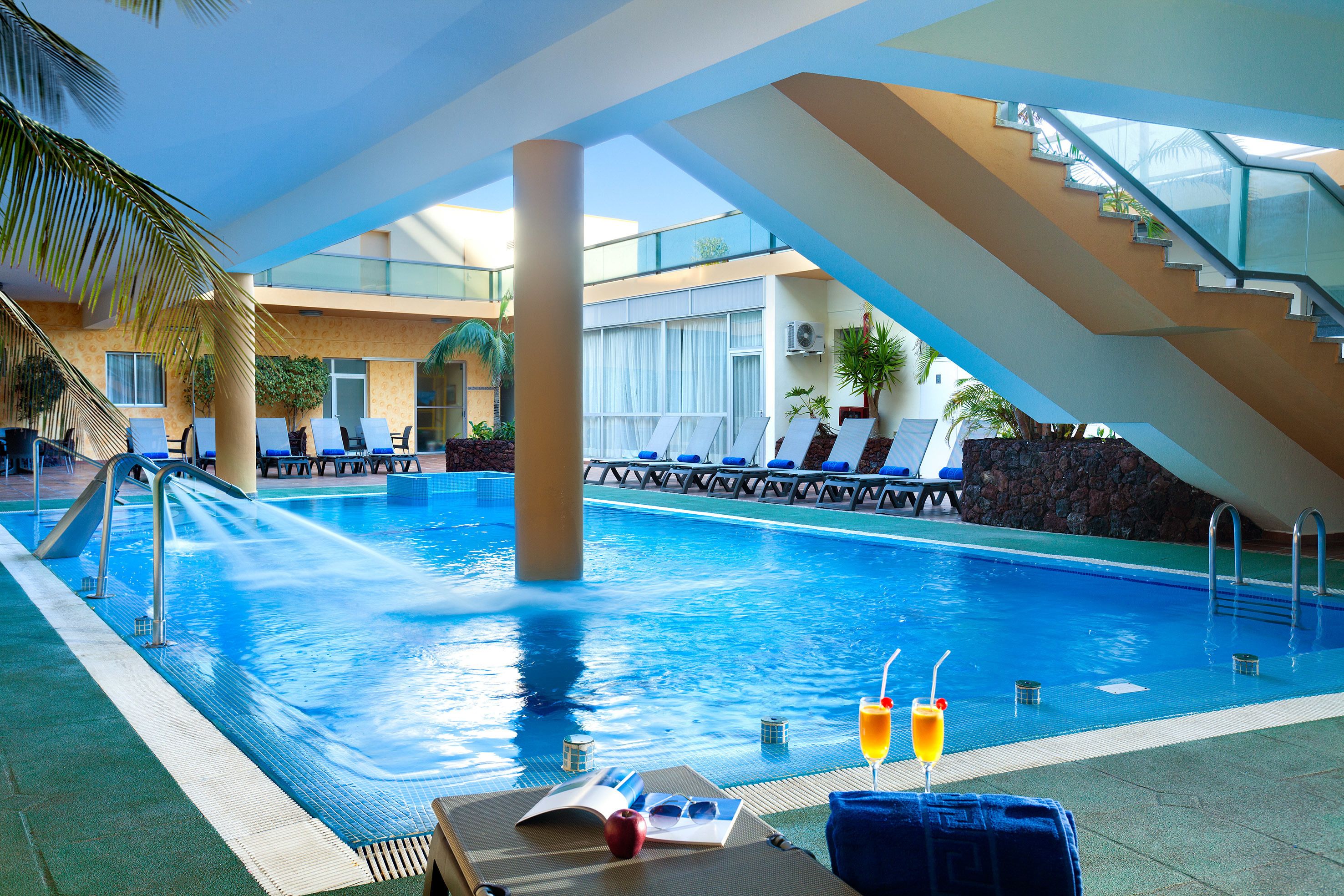 A pool area with lounge chairs, a water feature, and a staircase leading to an upper level.
