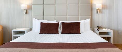 Una habitación de hotel con una cama grande, dos mesitas de noche, un cabecero acolchado y dos lámparas de pared.
